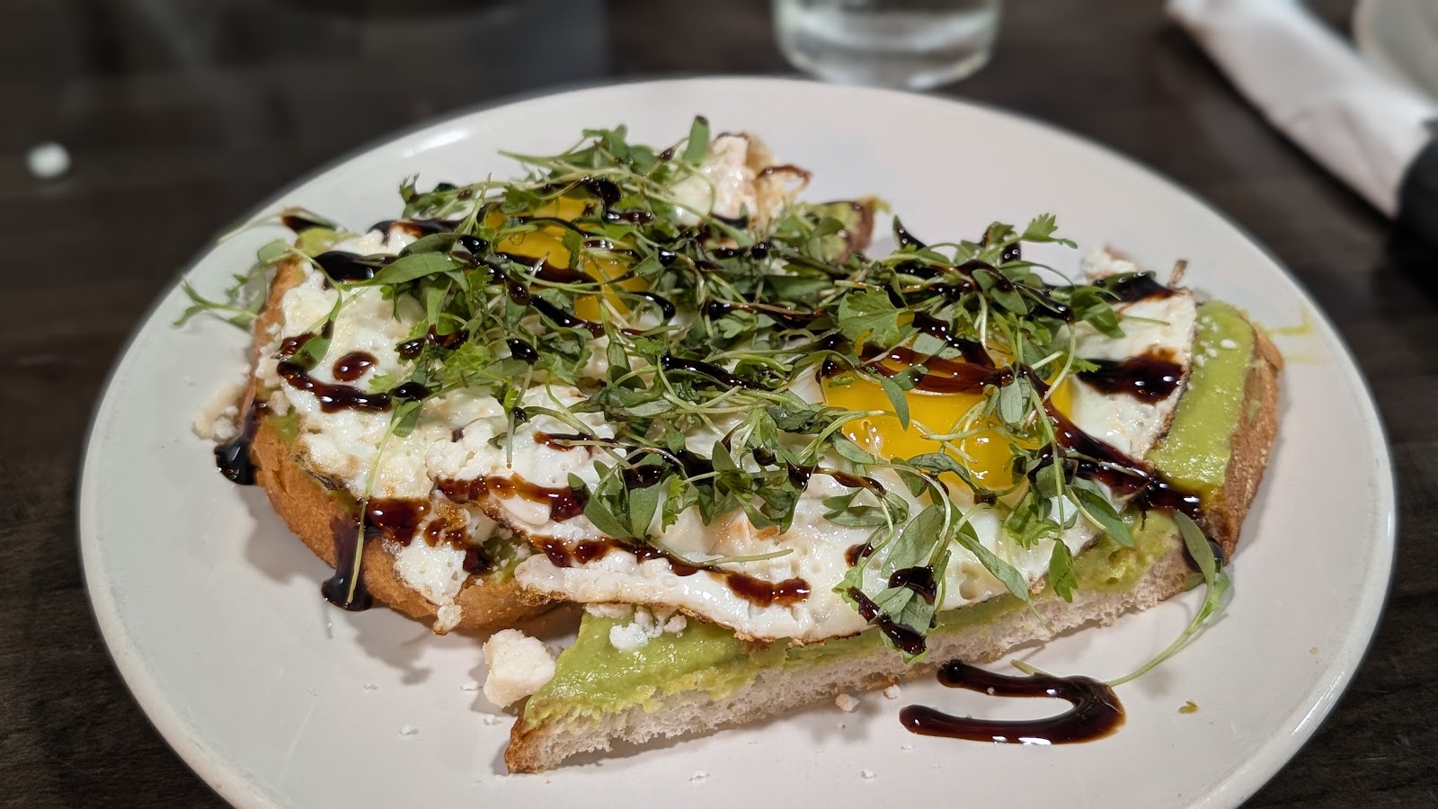 Avocado toast with fried egg, microgreens and balsamic drizzle